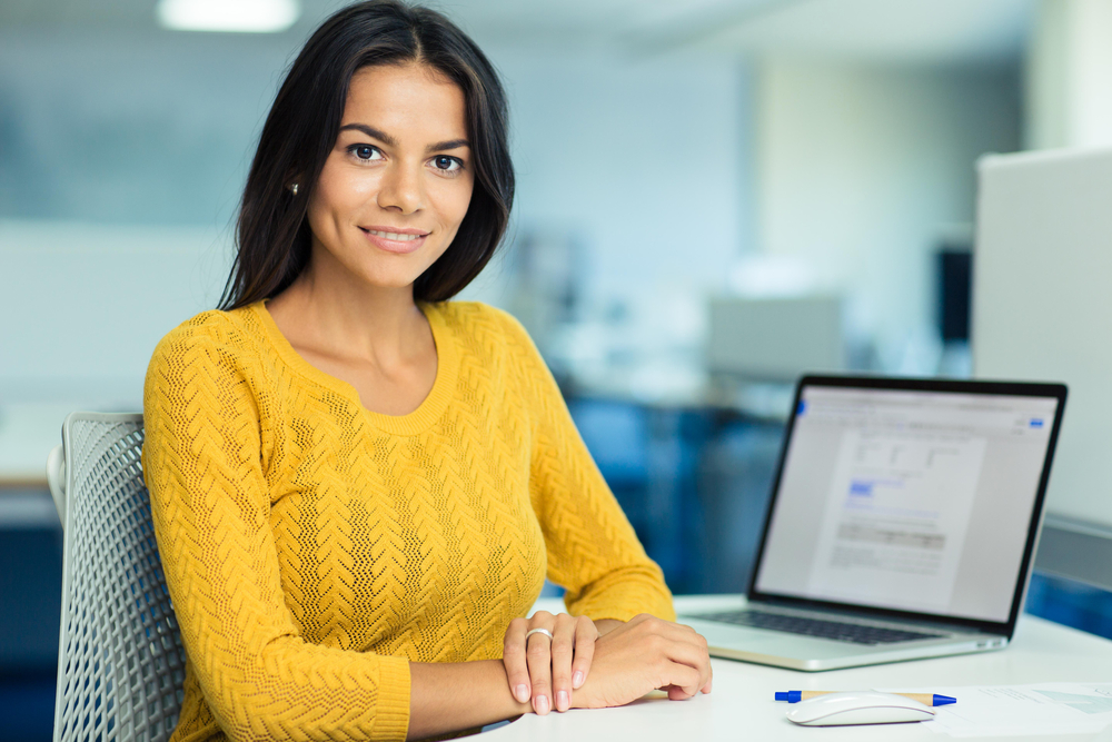 Portrait of a happy casual businesswoman in sweater sitting at her workplace in office Portrait of a happy casual businesswoman in sweater sitting at her workplace in office